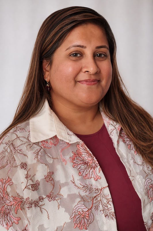 Maheen Hyder in a studio portrait, arms crossed, wearing a striped shirt